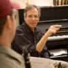 Frank Kowalsky sitting next to a piano teaching a studnet in the foreground that is wearing a baseball cap and holding a clarinet